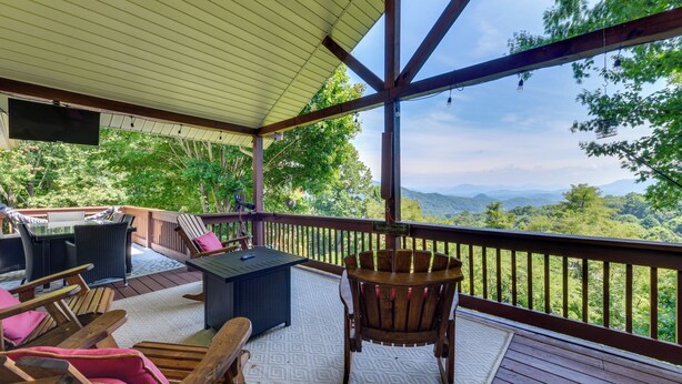 A covered outdoor deck with a table and chairs, a TV mounted on the ceiling, and a view of the mountains. - Pet-friendly Waynesville Retreat w/ Hot Tub! (Waynesville)