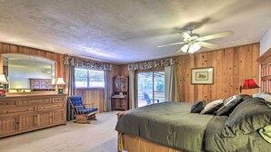A bedroom with a large bed, wooden walls, a ceiling fan, a dresser, a chair, and a window with curtains. - Charming Abode w/ Dock on the Suwannee River (Bell)
