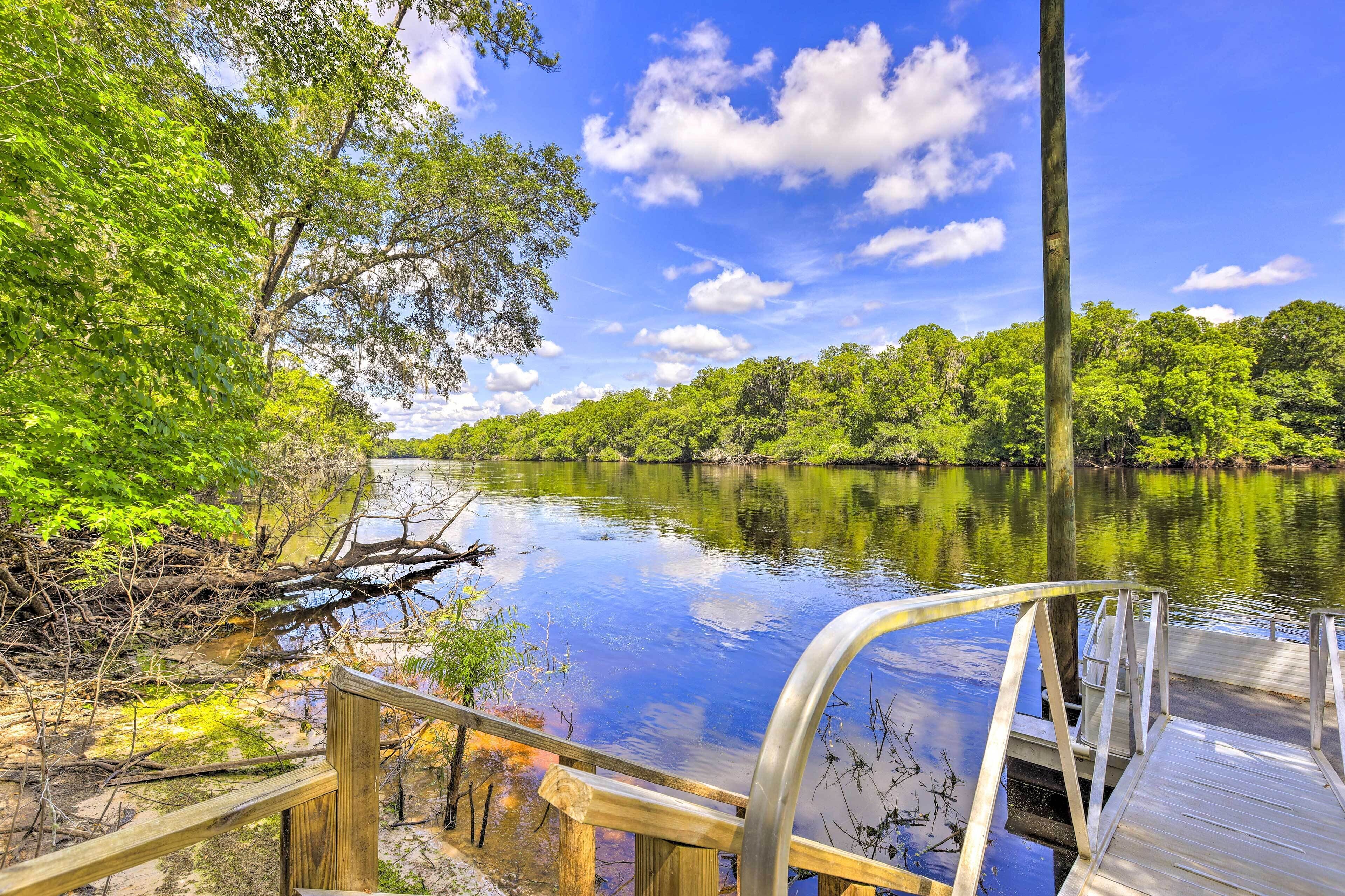 A wooden dock extending into a calm river surrounded by lush greenery.