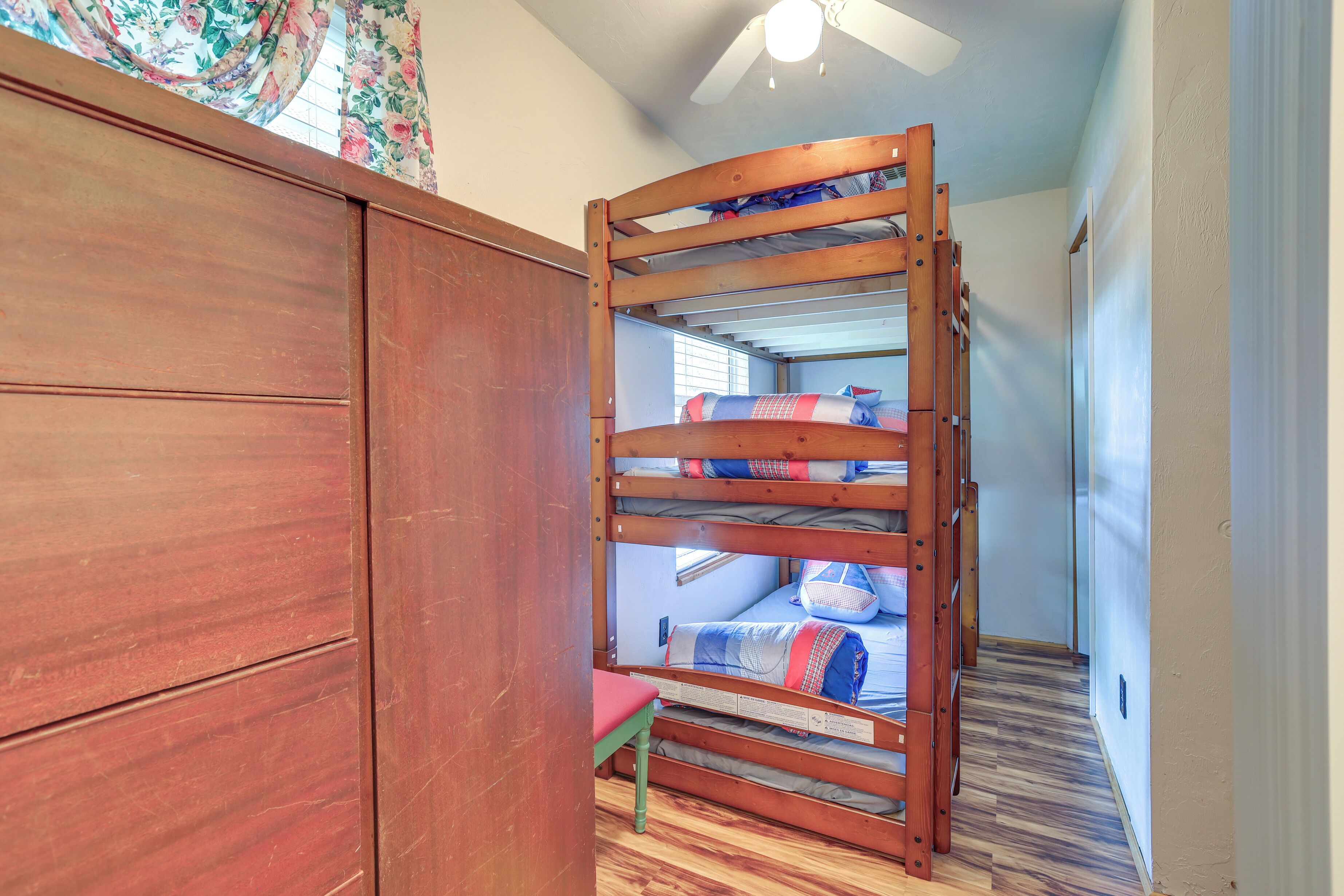 A bunk bed with a wooden frame, a small table, and a window with floral curtains.