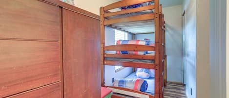 A bunk bed with a wooden frame, a small table, and a window with floral curtains.