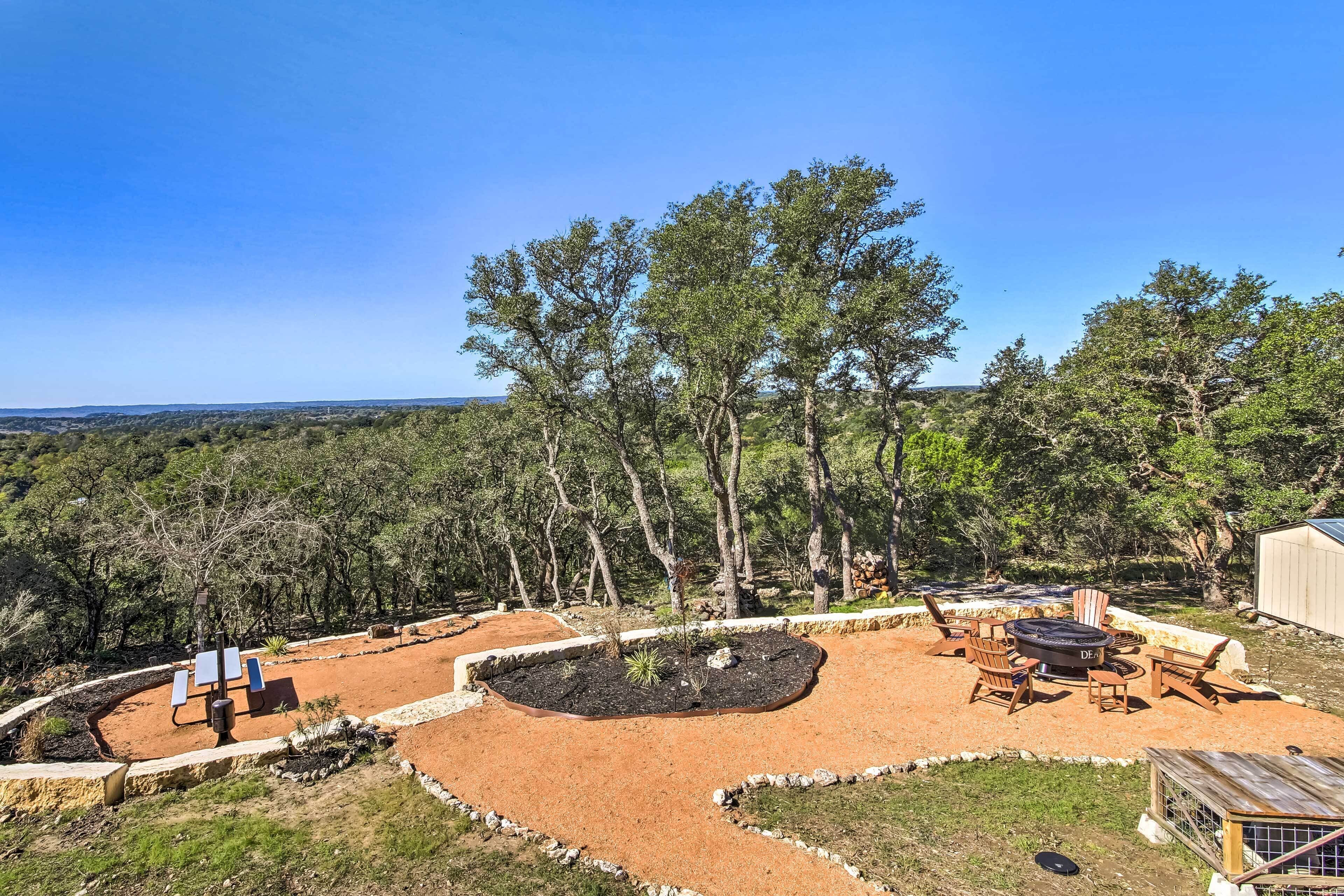 Un patio con mobiliario exterior, una fogata y vistas a un paisaje boscoso.