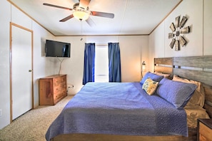 A bedroom with a bed, a ceiling fan, a TV, a wooden dresser, and a decorative wall piece.