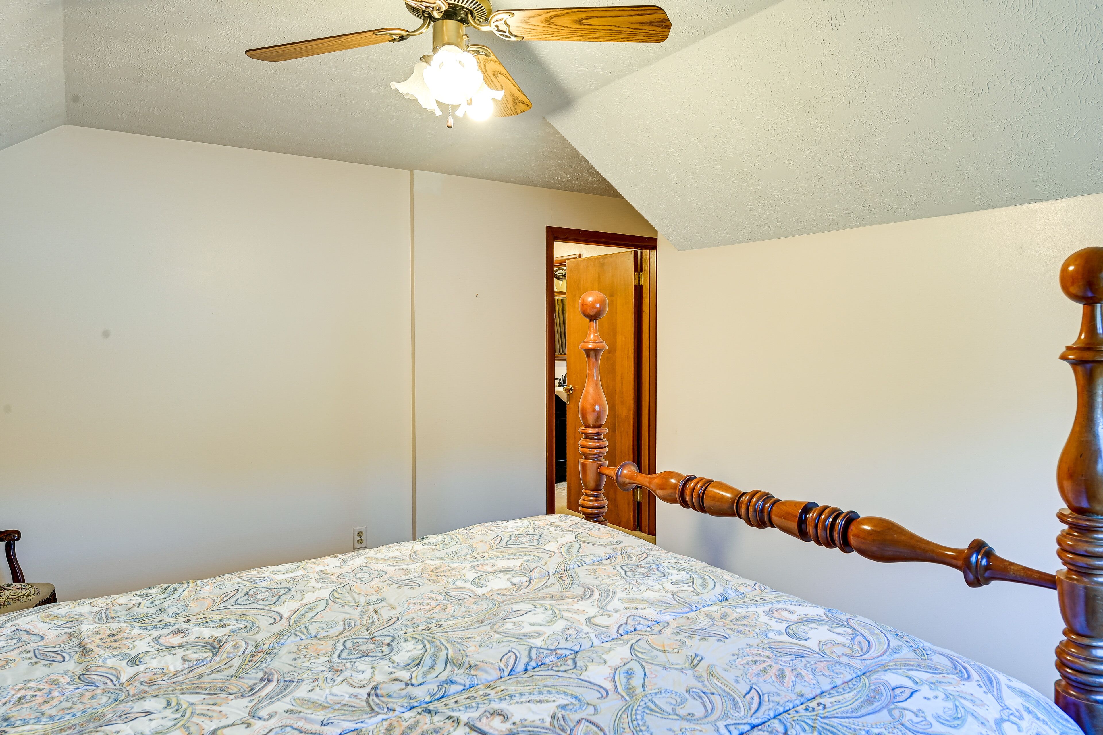 A bedroom with a wooden bed frame, a ceiling fan, and a patterned bedspread.