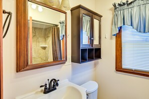 A bathroom with a white sink, a mirror, a toilet, and a window with blinds. - Downtown Paintsville Vacation Rental! (Paintsville)