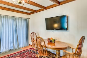 A dining area with a wooden table and chairs, a fruit bowl, and a television mounted on the wall. - Downtown Paintsville Vacation Rental! (Paintsville)