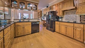 A spacious kitchen with wooden cabinets, a black refrigerator, and a dishwasher. - Family Retreat on Guadalupe River: 2 Living Areas! (Seguin)