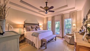 A bedroom with a large bed, a ceiling fan, a bench, a chair, and a desk with a lamp. - Family Retreat on Guadalupe River: 2 Living Areas! (Seguin)