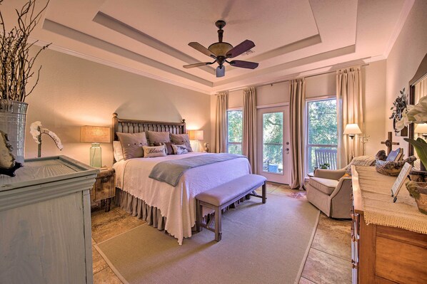 A bedroom with a large bed, a ceiling fan, a bench, a chair, and a desk with a lamp.