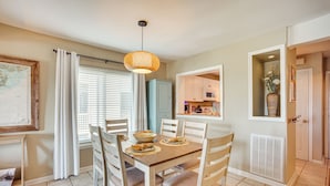 A dining area with a wooden table, chairs, and a hanging light fixture. - Harbor Island Condo With Deck - Steps to Beach! (Harbor Island)