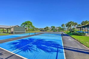 Una cancha de tenis con una red, rodeada por una cerca y palmeras.