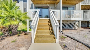 A wooden staircase leading to a balcony with white railings, a palm tree, and a clear sky. - Harbor Island Condo With Deck - Steps to Beach! (Harbor Island)