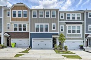 A row of townhouses with attached garages, a front lawn, and a clear sky. - Sleek Durham Townhome Near Dtwn w/ Balcony! (Durham)