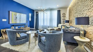 A modern living room with a blue accent wall, a large chandelier, and a leather sofa. - Sleek Durham Townhome Near Dtwn w/ Balcony! (Durham)