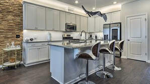 A modern kitchen with white cabinetry, a central island with bar stools, stainless steel appliances, and a unique ceiling light fixture. - Sleek Durham Townhome Near Dtwn w/ Balcony! (Durham)