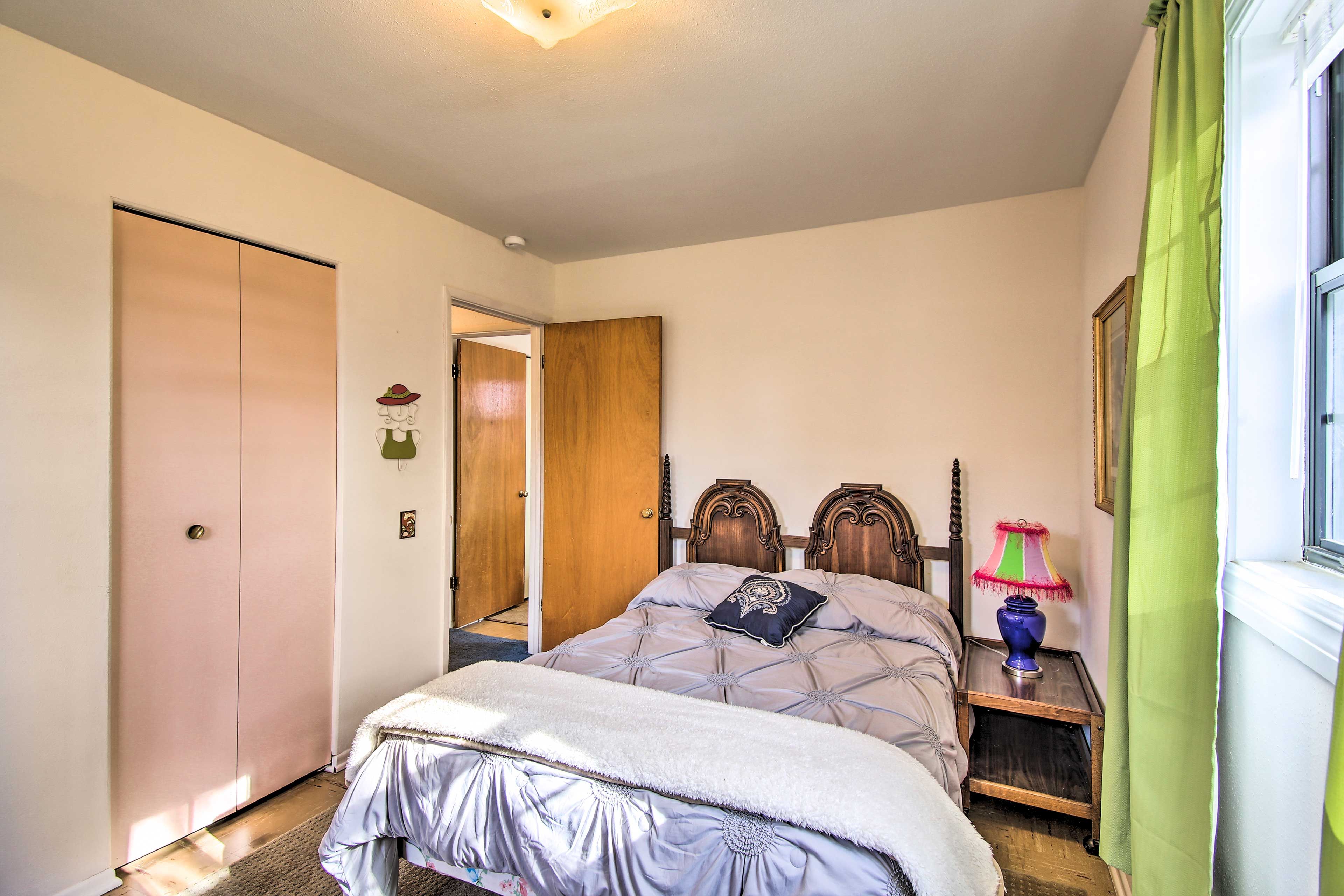 A bedroom with a bed, a nightstand, a lamp, a door, and a window with curtains.