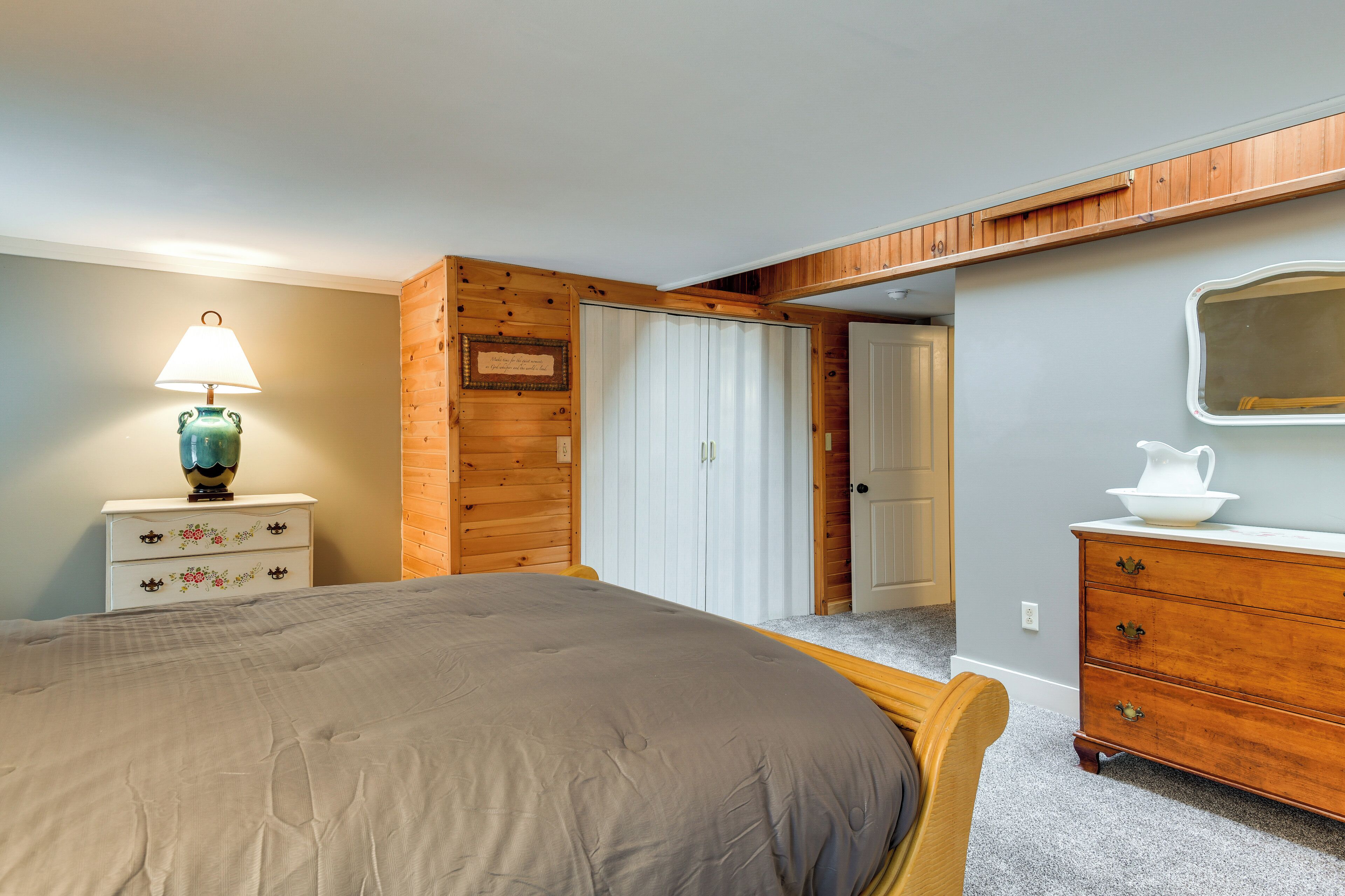 Een slaapkamer met een bed, een kaptafel, nachtkastje, lamp en een deur naar een andere kamer.