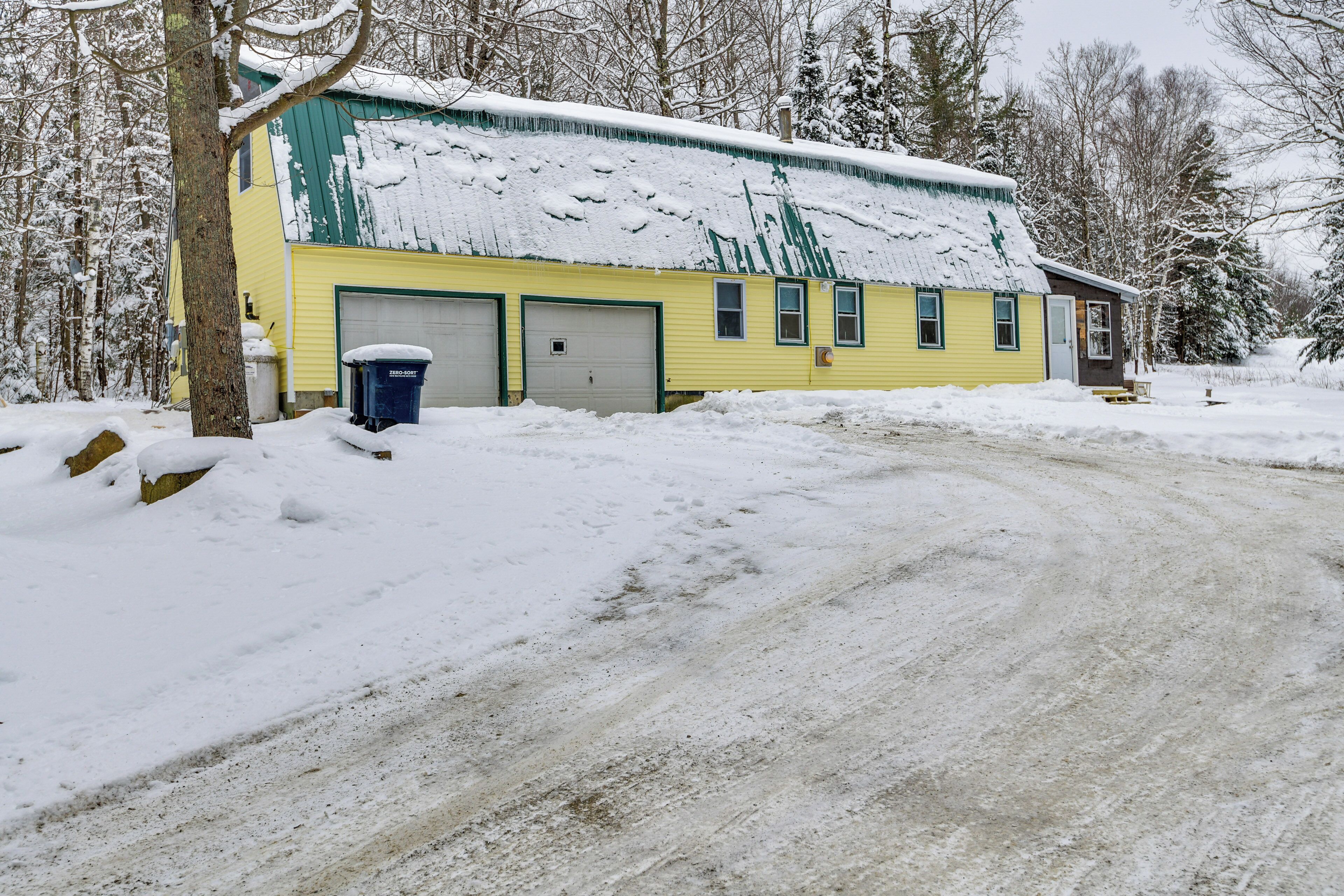 A yellow building with a snow-covered roof, a garage, and a small porch.