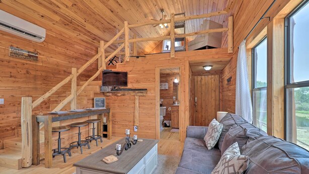 A wooden cabin interior with a sofa, a coffee table, a TV, and a staircase.