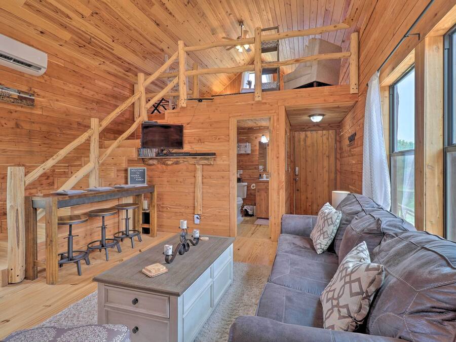 A wooden cabin interior with a sofa, a coffee table, a TV, and a staircase.