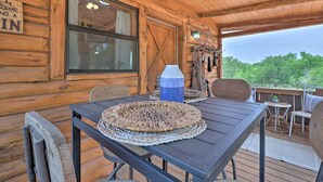 A wooden cabin with a table and chairs, a window, and a view of trees.