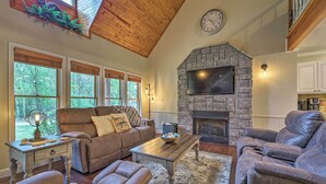 A living room with a stone fireplace, wooden ceiling, and large windows. - Updated Cabin on White River by Boat Landing! (Calico Rock)