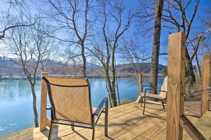 Une terrasse en bois, agrémentée de chaises, qui offre une vue sur un lac paisible, le tout entouré d’arbres.