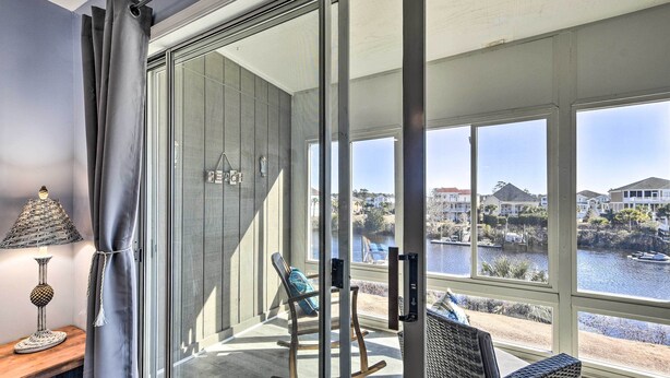 A balcony with a view of a lake and houses, a rocking chair, and a lamp on a wooden table. - ~ 2 Mi to Cherry Grove Beach: Little River Condo (Little River)