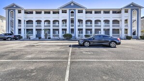 A multi-story hotel with a central entrance, balconies, and a parking lot with cars. - ~ 2 Mi to Cherry Grove Beach: Little River Condo (Little River)