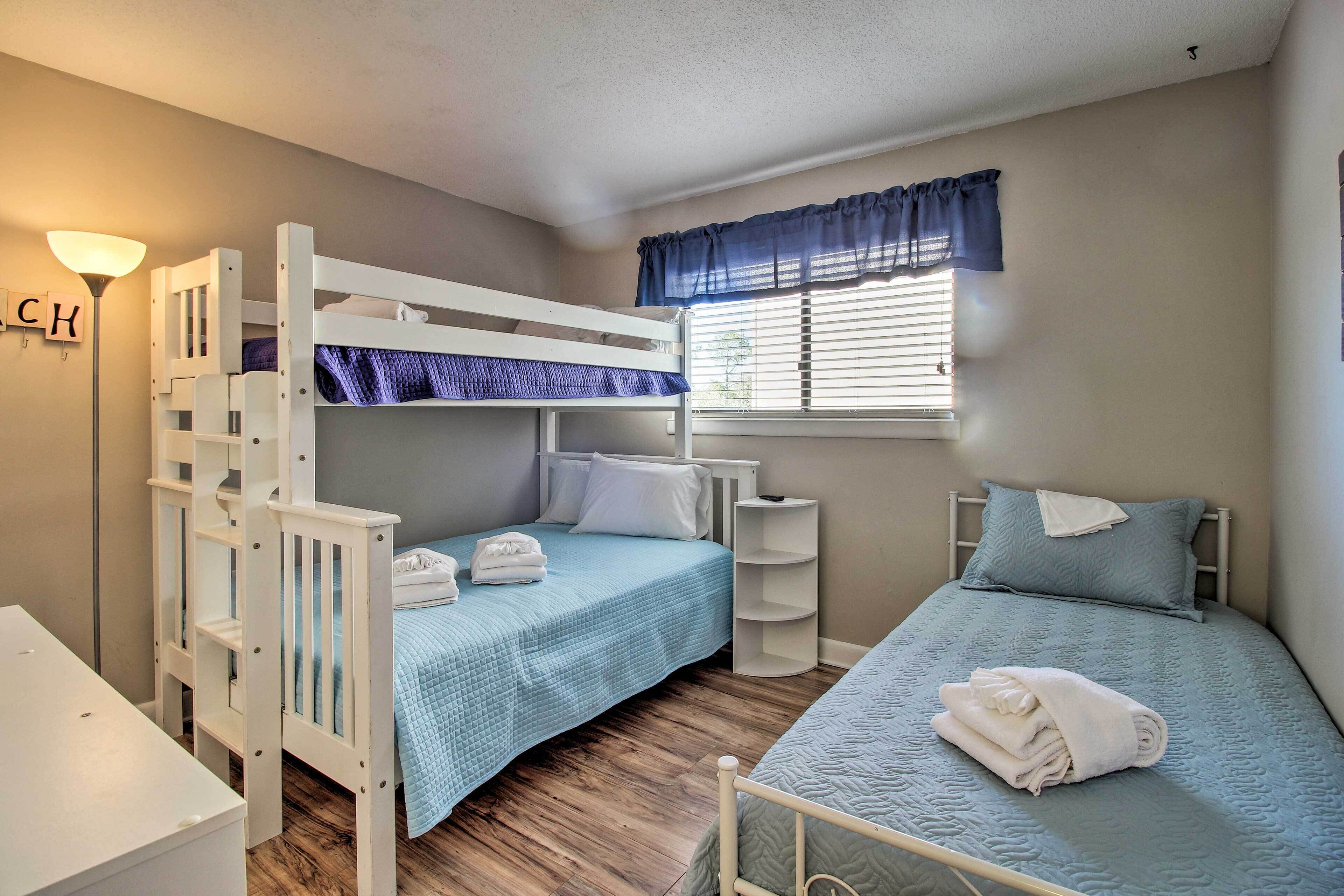A bedroom with bunk beds, a bedside table, a lamp, and a window with curtains.