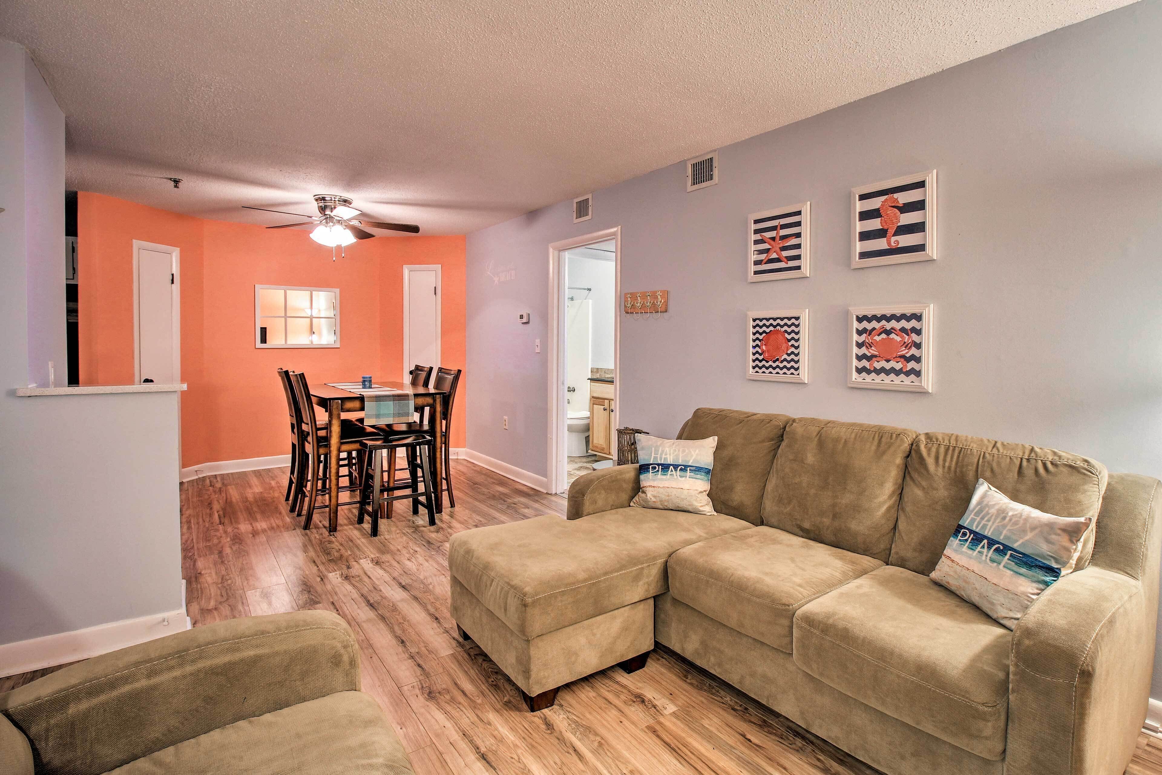 A living room with a beige sectional sofa, a dining table with chairs, and a ceiling fan.