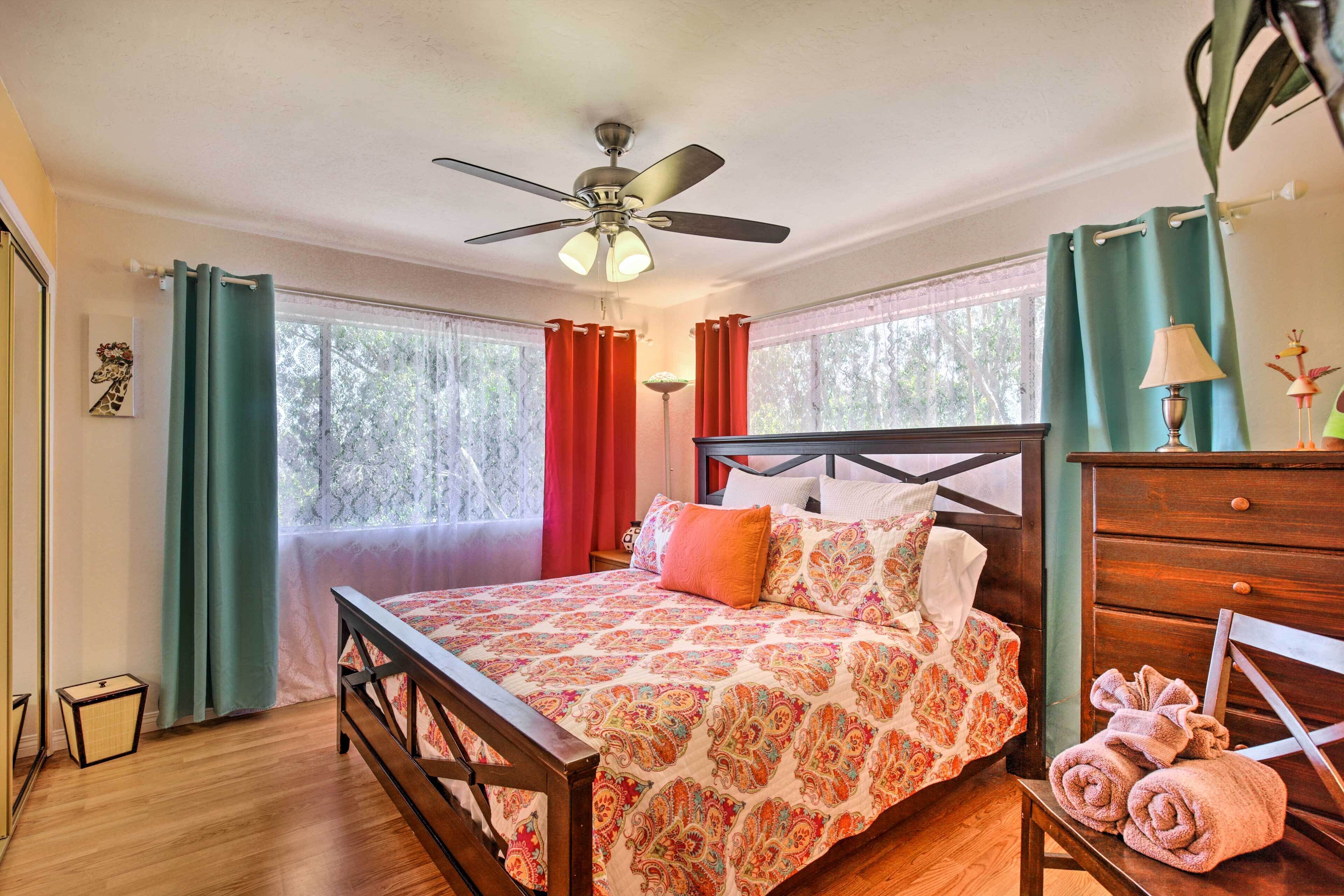 A bedroom with a wooden bed, a ceiling fan, and a view of trees through the window.
