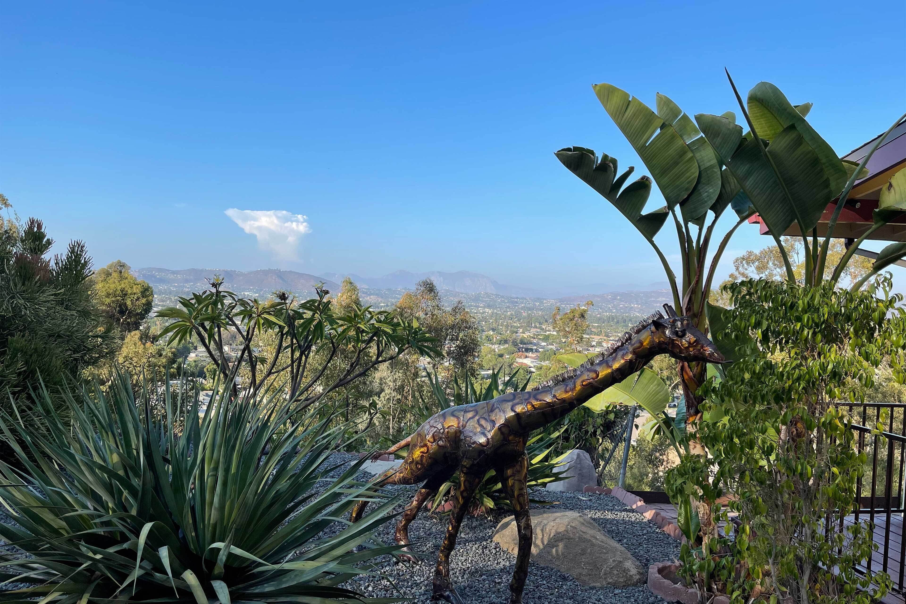 Eine Dinosaurierskulptur in einem Garten mit Blick auf ferne Berge und einem klaren Himmel.