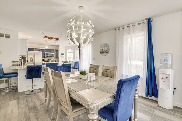 A modern kitchen with a dining area, a water dispenser, and a large decorative light fixture.