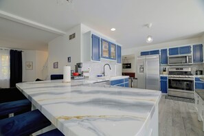 A modern kitchen with a marble island, blue cabinets, stainless steel appliances, and a large window. - Fire Pit + Hot Tub: Peaceful Poconos Farms Getaway (Tobyhanna)