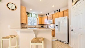 A kitchen with wooden cabinets, a white refrigerator, a microwave, a sink, and two wicker stools. - Kissimmee Getaway ~ 4 Mi to Walt Disney World (Kissimmee)