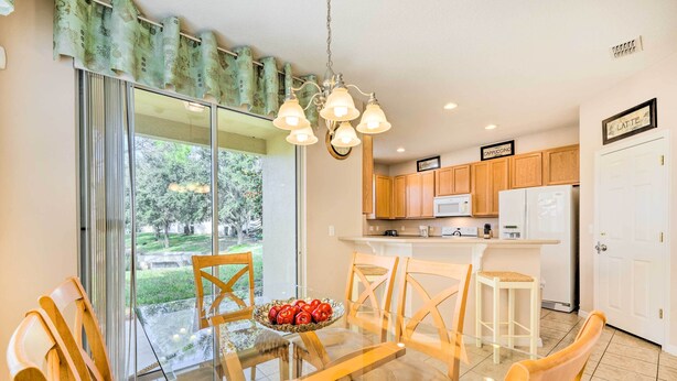 A modern kitchen with wooden cabinets, a white refrigerator, and a glass dining table with chairs. - Kissimmee Getaway ~ 4 Mi to Walt Disney World (Kissimmee)