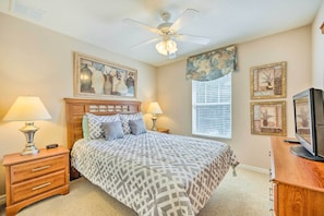 A bedroom with a bed, two bedside tables with lamps, a ceiling fan, and artwork on the walls.