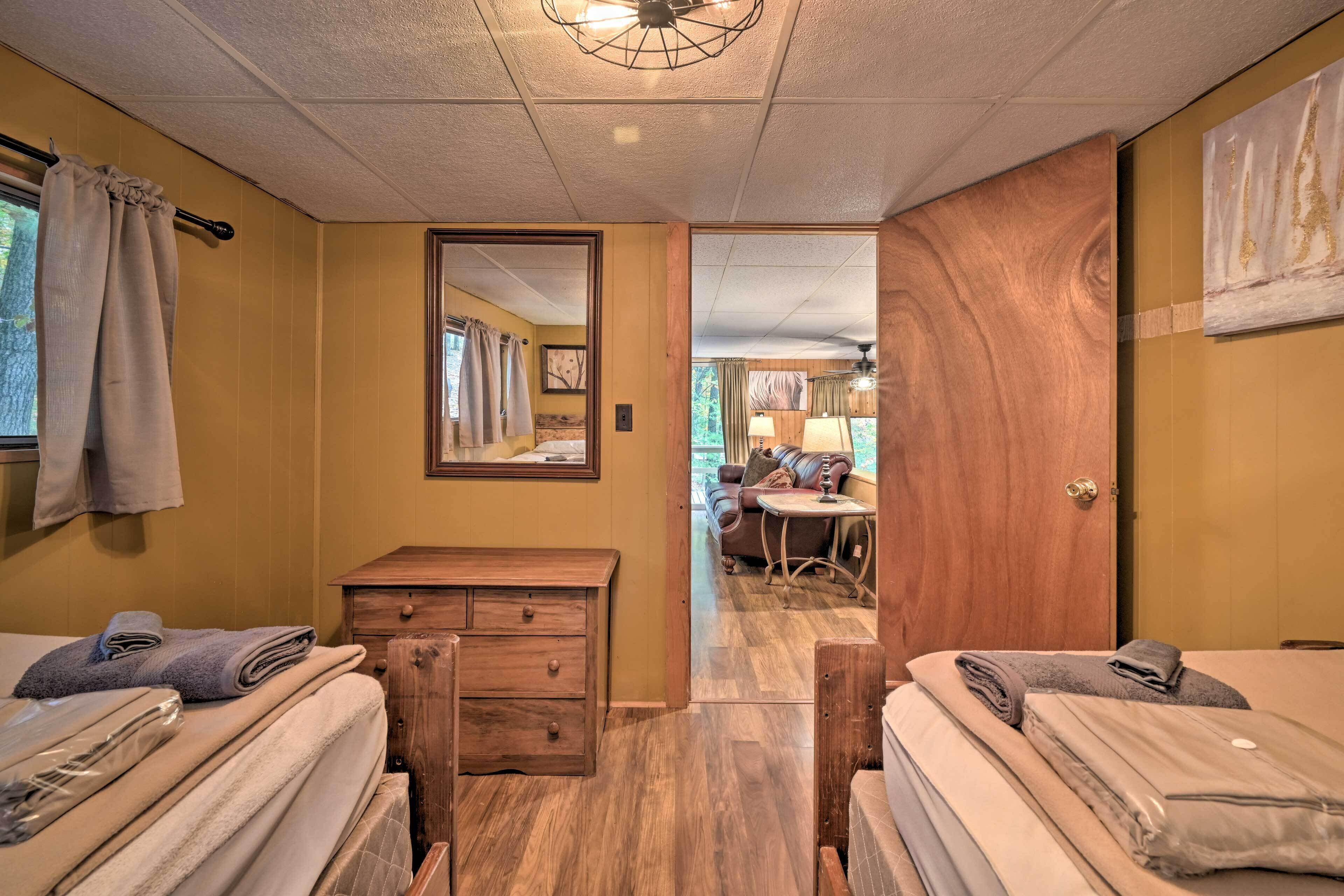 A hotel room with two beds, a wooden dresser, a mirror, and a view into the living area.