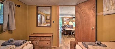 A hotel room with two beds, a wooden dresser, a mirror, and a view into the living area.