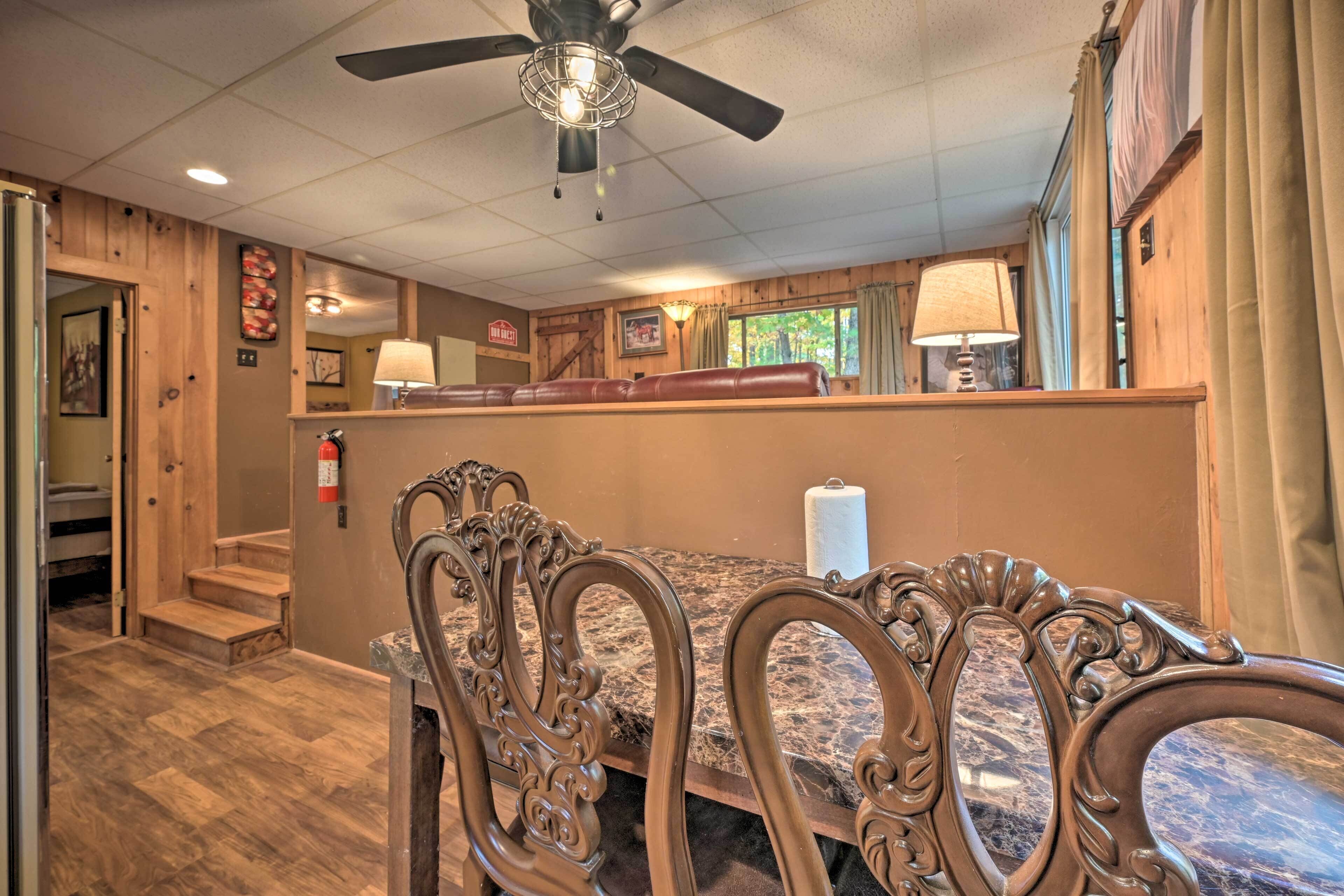 A dining area with a wooden table and chairs, a ceiling fan, and a view of the outdoors through a window.