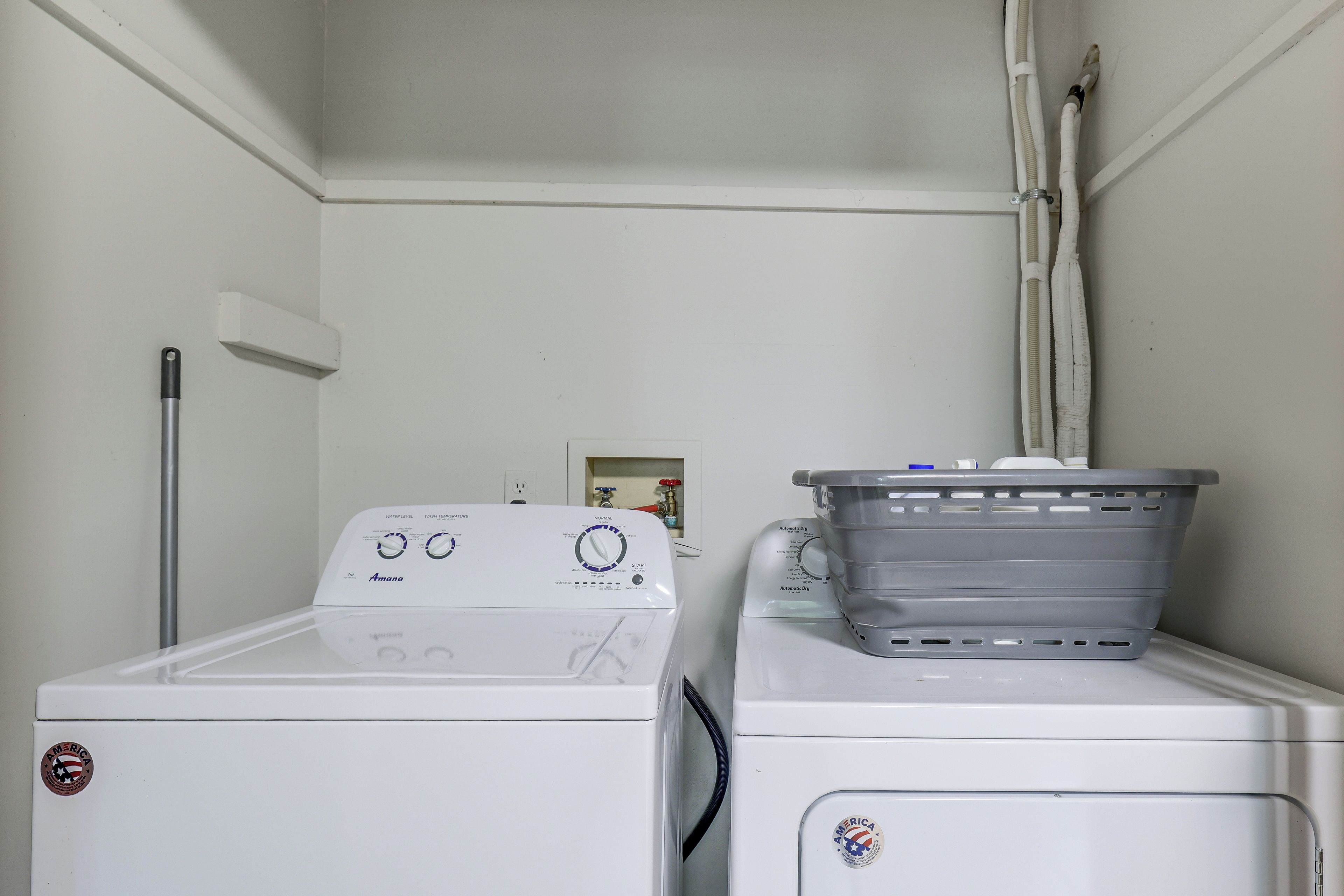 A laundry room with two stacked washers and dryers, a utility pole, and a laundry basket on the dryer.