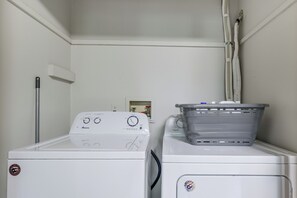 A laundry room with two stacked washers and dryers, a utility pole, and a laundry basket on the dryer. - Hot Tub + Game Room: Peaceful Poconos Home! (Lake Harmony)