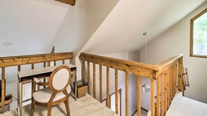 Una habitación con un escritorio de madera, una silla y un ventanal pequeño.