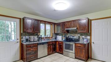 Une cuisine avec des meubles de rangement en bois, un lave-vaisselle, une cuisinière et une fenêtre.