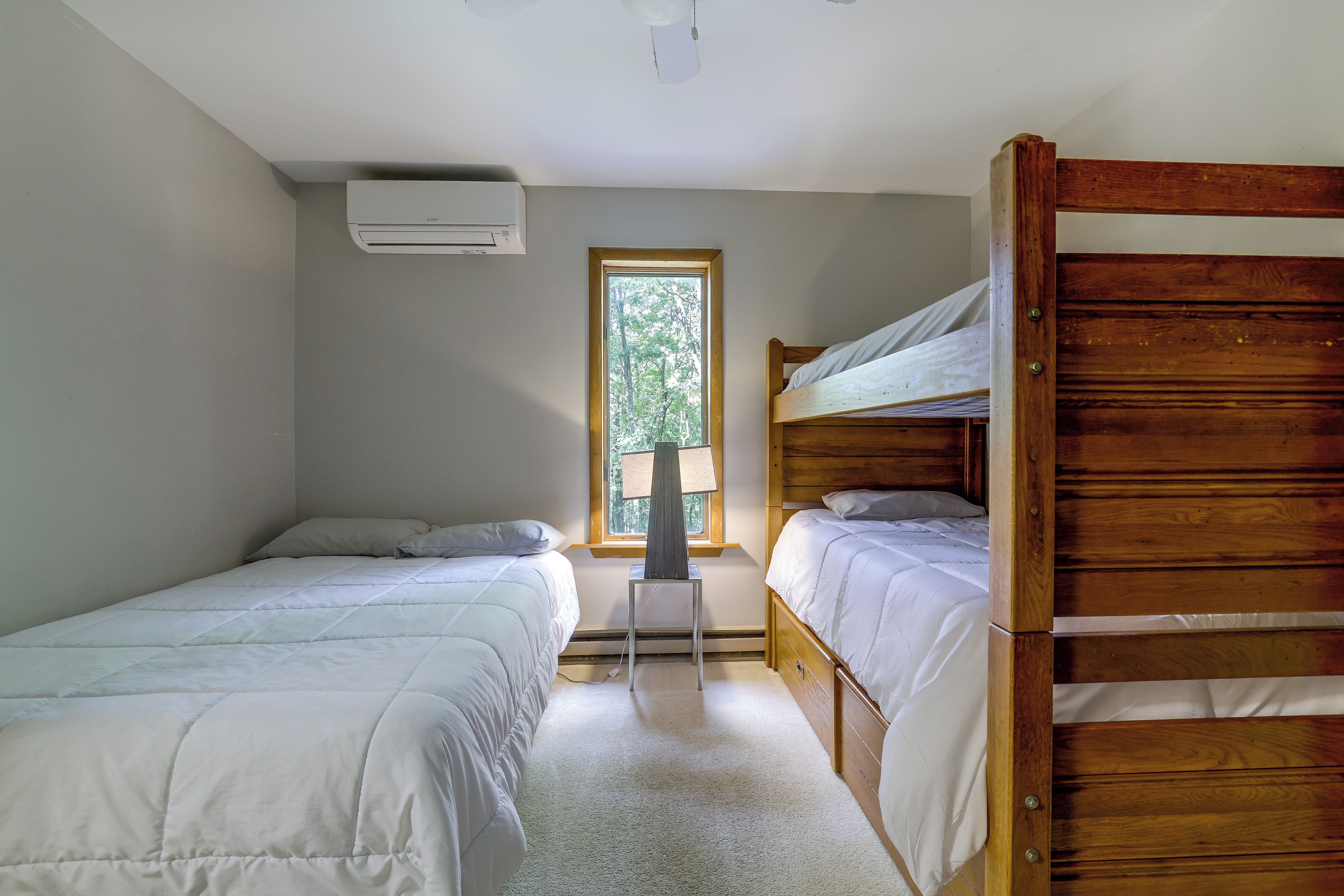 Un dormitorio con dos camas individuales, una ventana y aire acondicionado instalado en la pared.