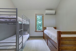 Ein Schlafsaalzimmer mit Etagenbetten, einem Fenster mit Blick auf Bäume und einer Klimaanlage an der Wand.