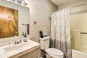 Un baño con lavamanos blanco, espejo, inodoro y cortina de ducha.