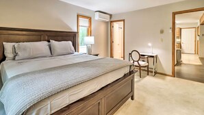 A bedroom with a large bed, a bedside table with a lamp, a chair, and an air conditioning unit. - Hot Tub + Game Room: Peaceful Poconos Home! (Lake Harmony)