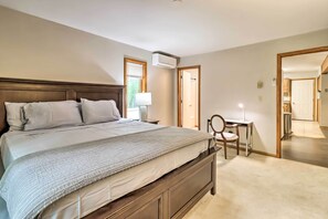 Un dormitorio con una cama grande, una mesita de noche con lámpara, una silla y un equipo de aire acondicionado.